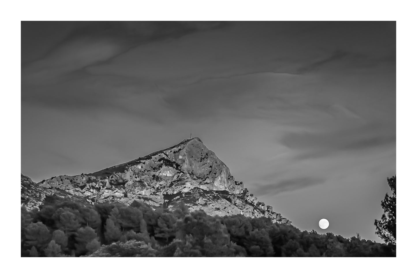 Lune jaune se levant près de la montagne Sainte-Victoire, ciel bleu aux nuages roses, pins en premier plan au crépuscule, noir et blanc avec bordure