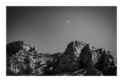 Demi-lune au-dessus des crêtes calcaires de Sugiton, ciel bleu profond et relief minéral, noir et blanc avec bordure