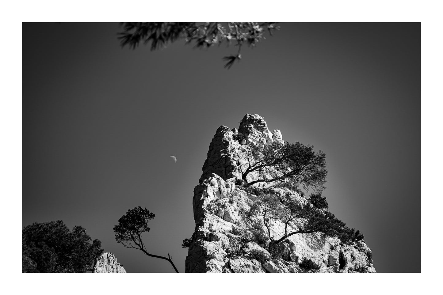 Piton rocheux et pins, demi-lune en arrière-plan, interprétation noir et blanc avec bordure
