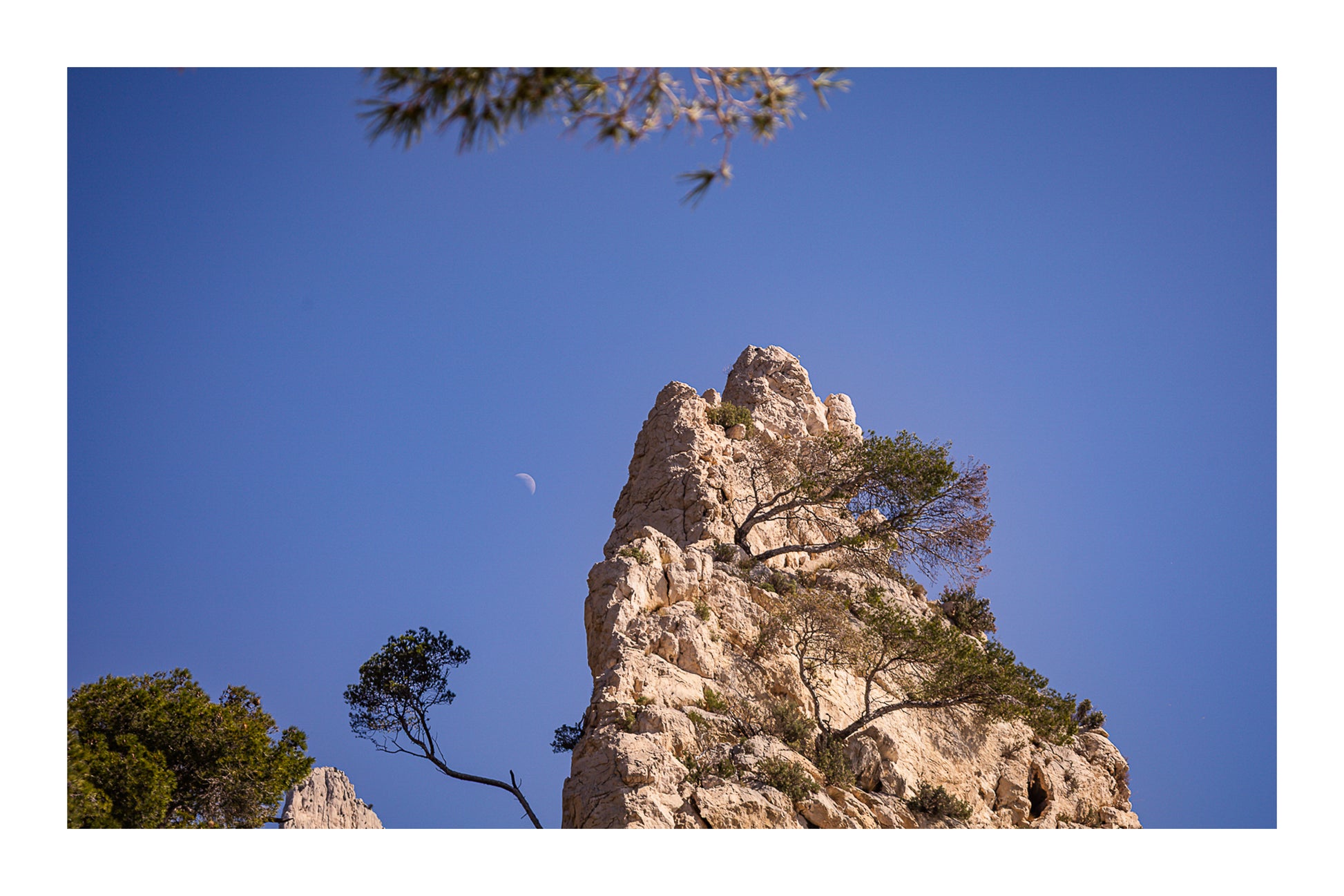 Piton calcaire et pins à Sugiton avec la demi-lune dans un ciel bleu clair avec bordure
