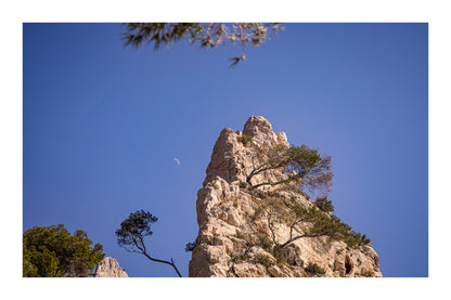 Piton calcaire et pins à Sugiton avec la demi-lune dans un ciel bleu clair avec bordure