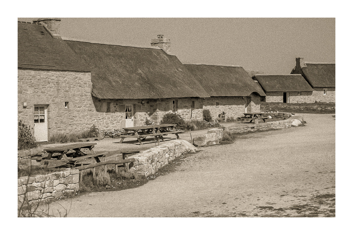 Longère de Meneham avec tables en bois, mur de pierre et toit de chaume, traitement vintage sépia - Kerlouan, Finistère, avec bordure