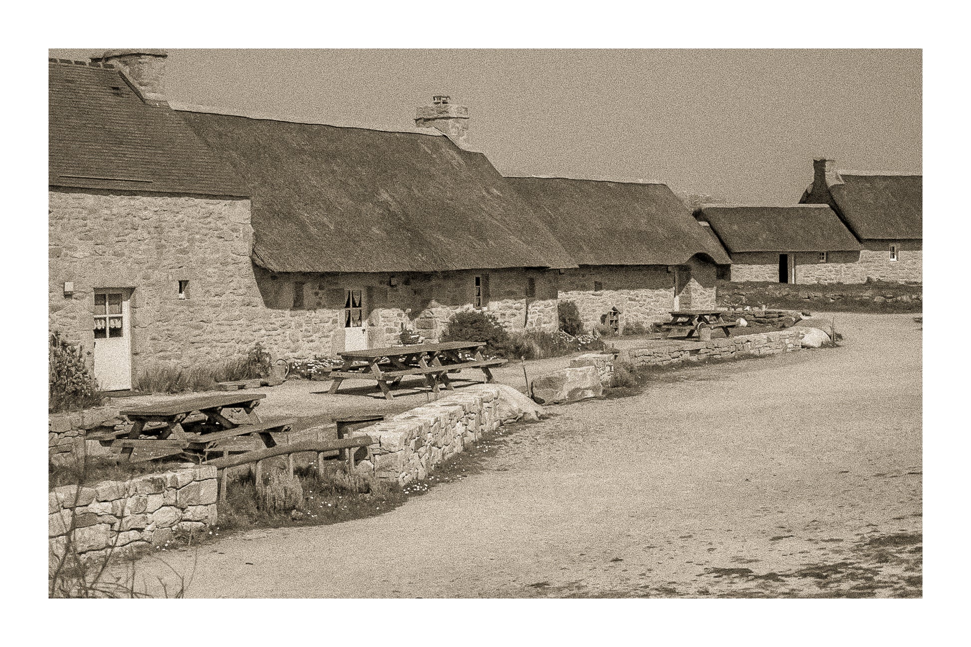 Longère de Meneham avec tables en bois, mur de pierre et toit de chaume, traitement vintage sépia - Kerlouan, Finistère, avec bordure