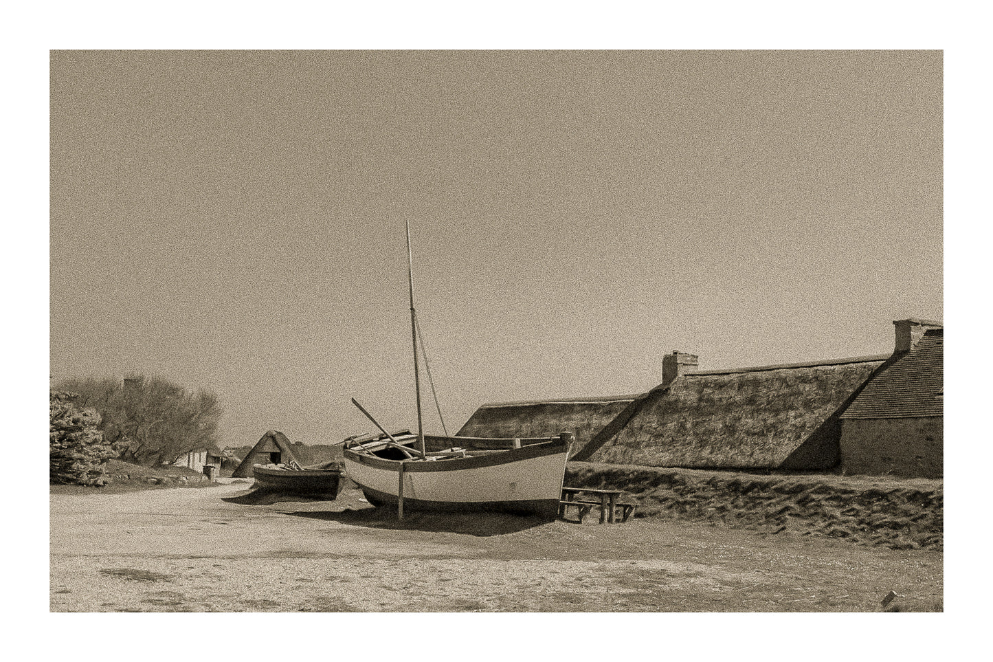 Barques tirées au sec devant les toits de chaume et murets de pierre à Meneham, ambiance ancienne en sépia avec bordure