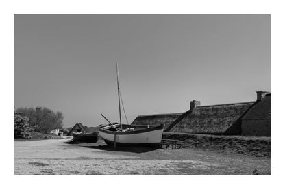 Barques tirées au sec devant les toits de chaume et murets de pierre à Meneham, ambiance ancienne, noir et blanc avec bordure