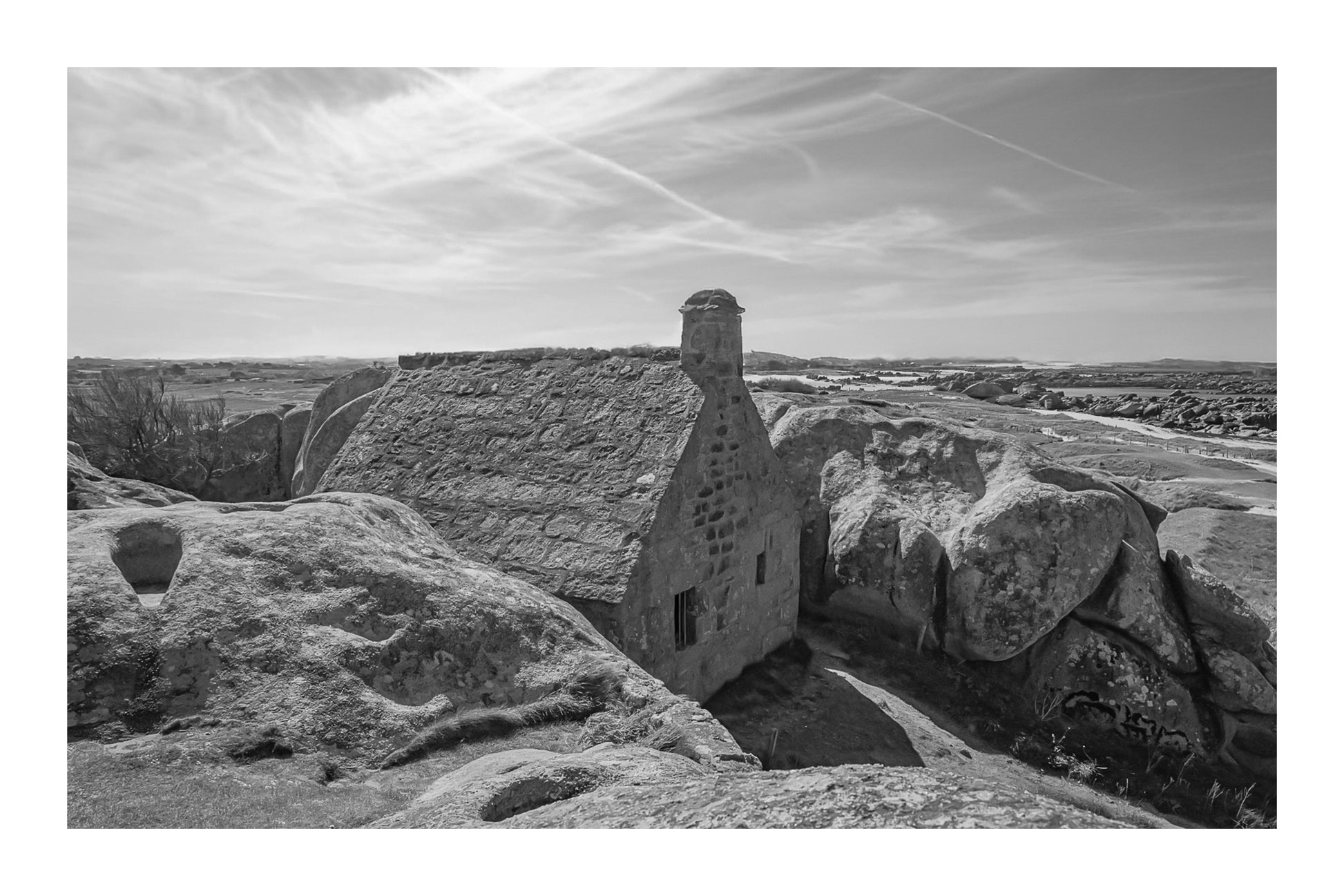 La maison emblématique de Meneham nichée entre deux énormes blocs de granit, vue d’ensemble, noir et blanc avec bordure