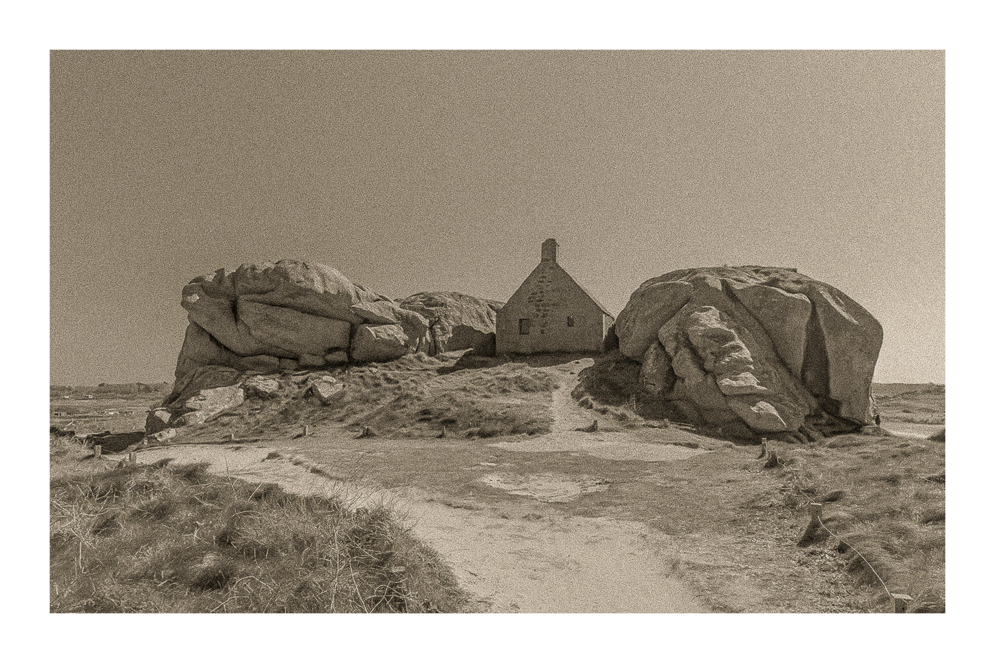 Façade de la maison des gardes encadrée par deux rochers monumentaux, Meneham (Kerlouan), traitement sepia avec bordure