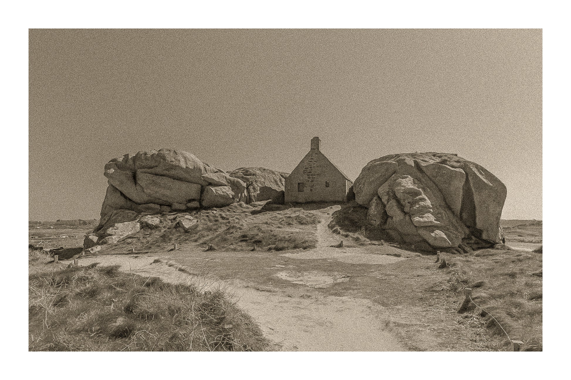 Façade de la maison des gardes encadrée par deux rochers monumentaux, Meneham (Kerlouan), traitement sepia avec bordure