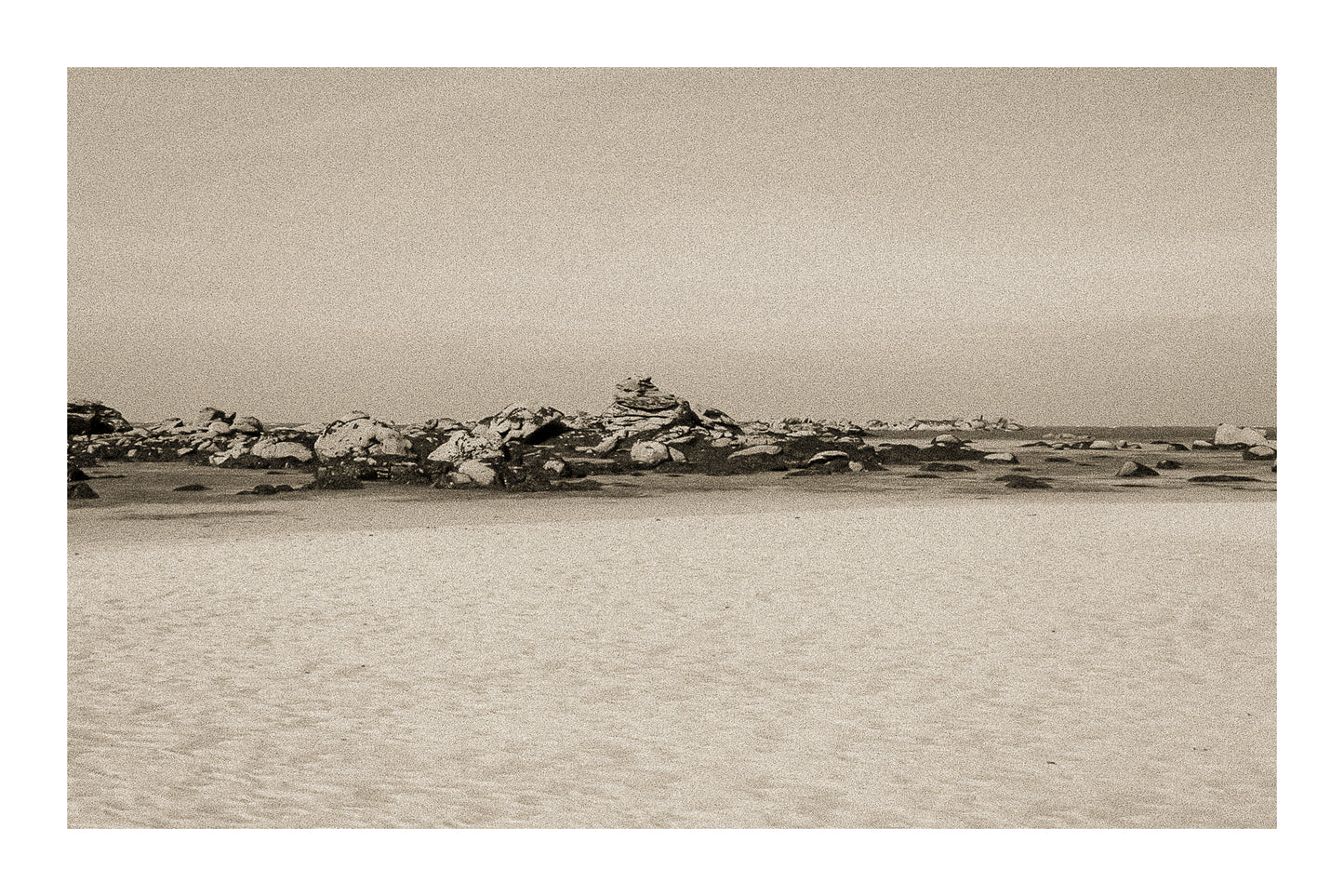 Grande plage claire avec rochers épars et ligne d’horizon marine, ambiance sépia vintage avec bordure à Meneham