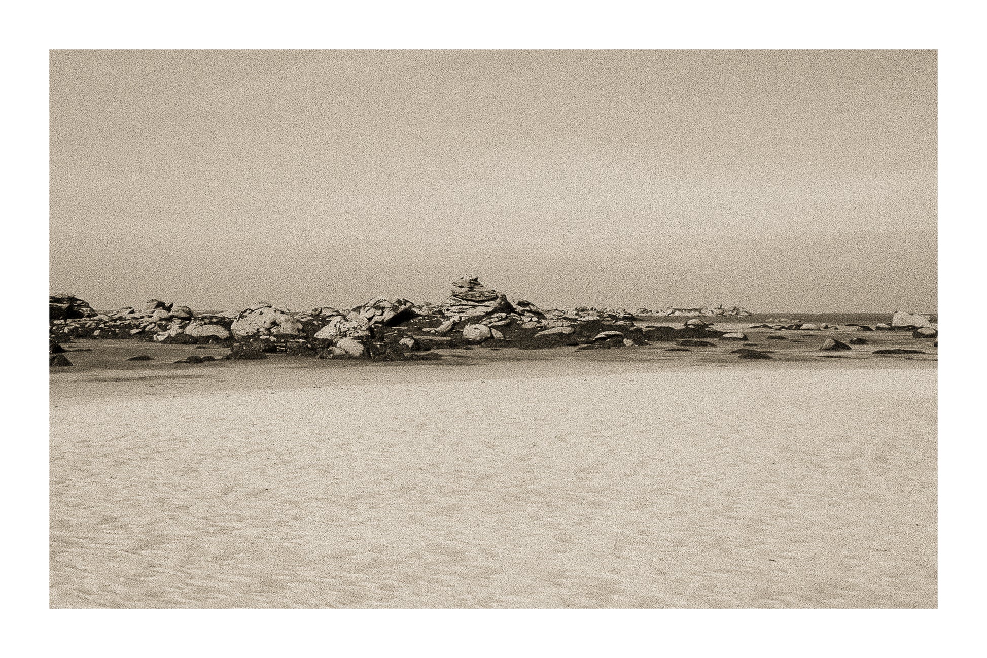 Grande plage claire avec rochers épars et ligne d’horizon marine, ambiance sépia vintage avec bordure à Meneham