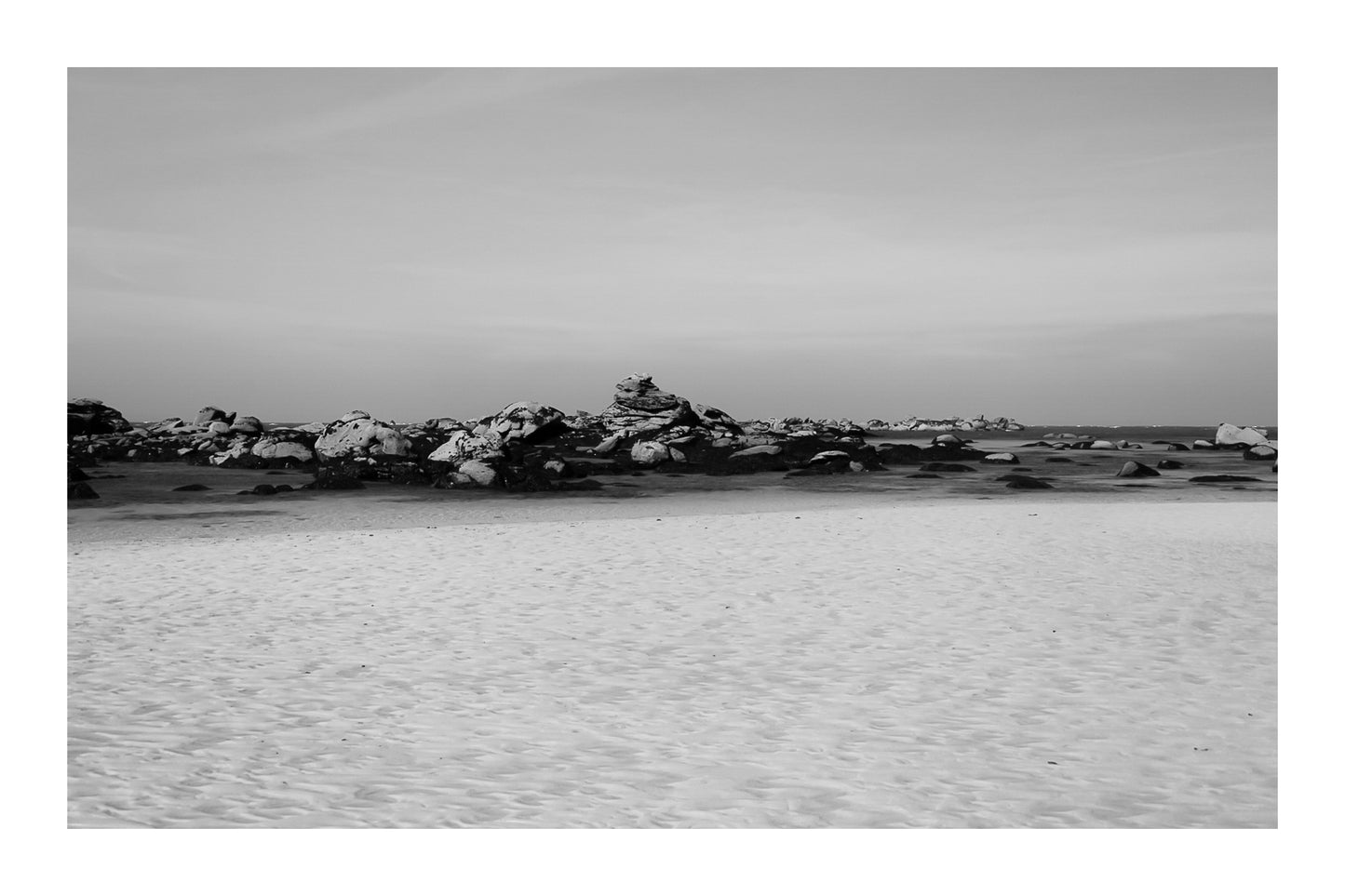Grande plage claire avec rochers épars et ligne d’horizon marine, noir et blanc avec bordure à Meneham