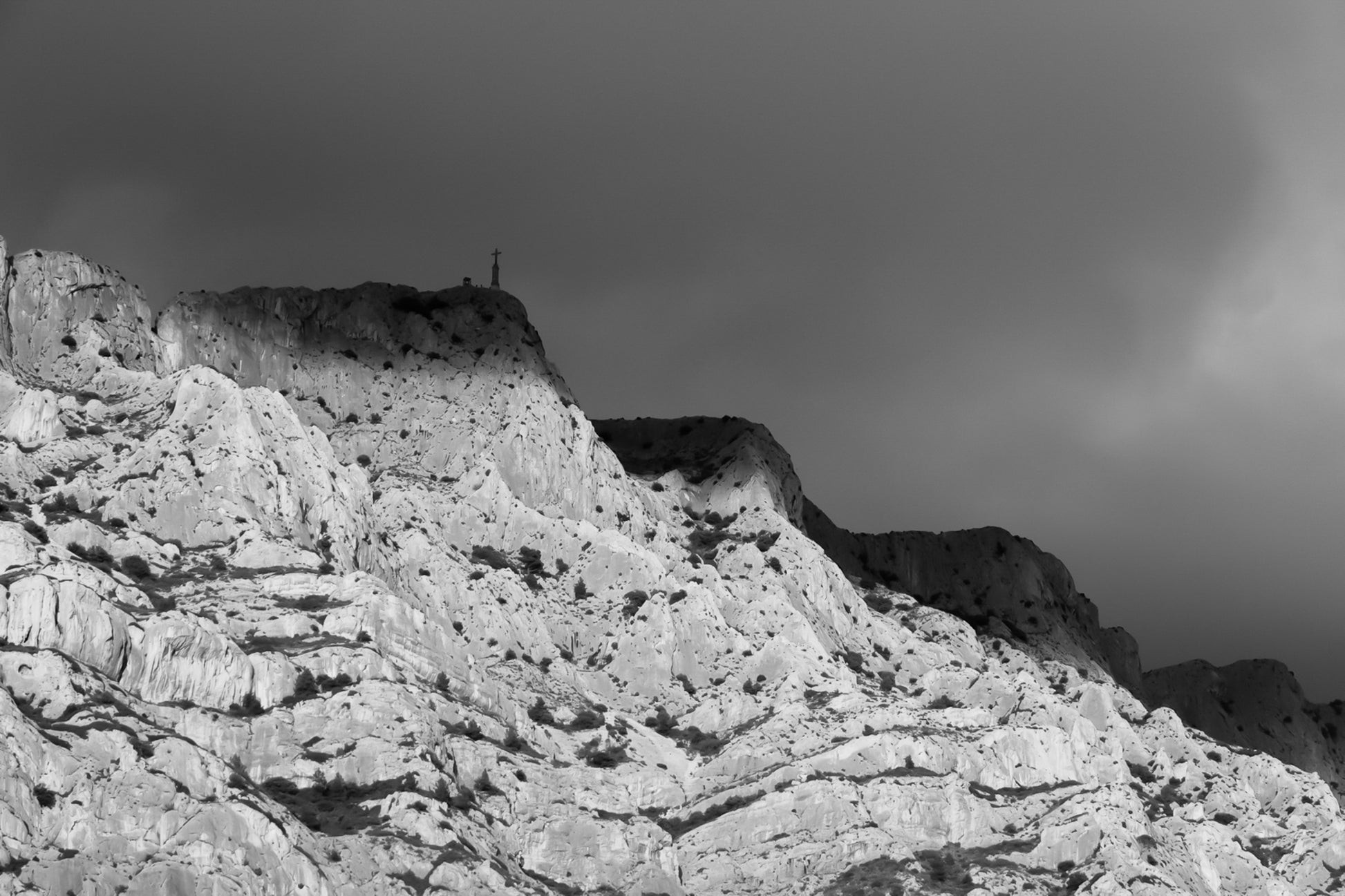 Croix de la Sainte-Victoire éclairée par le soleil sur fond de nuages sombres, noir et blanc