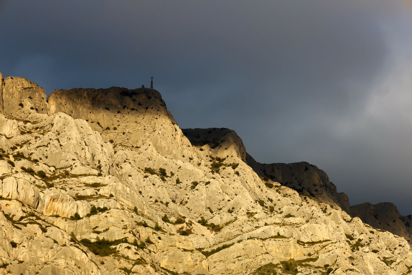 Croix de la Sainte-Victoire éclairée par le soleil sur fond de nuages sombres
