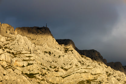 Croix de la Sainte-Victoire éclairée par le soleil sur fond de nuages sombres
