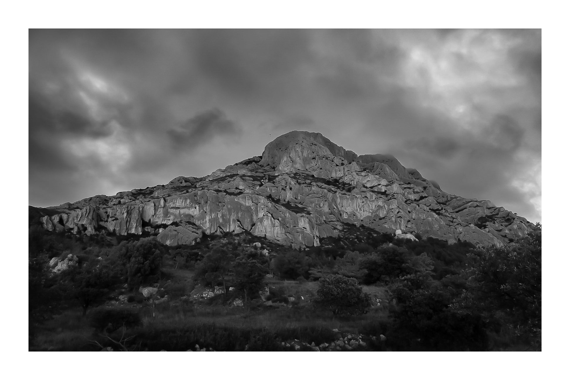 Montagne Sainte-Victoire sous un ciel d’orage vert et violet, vue depuis le pied de la falaise, noir et blanc avec bordure