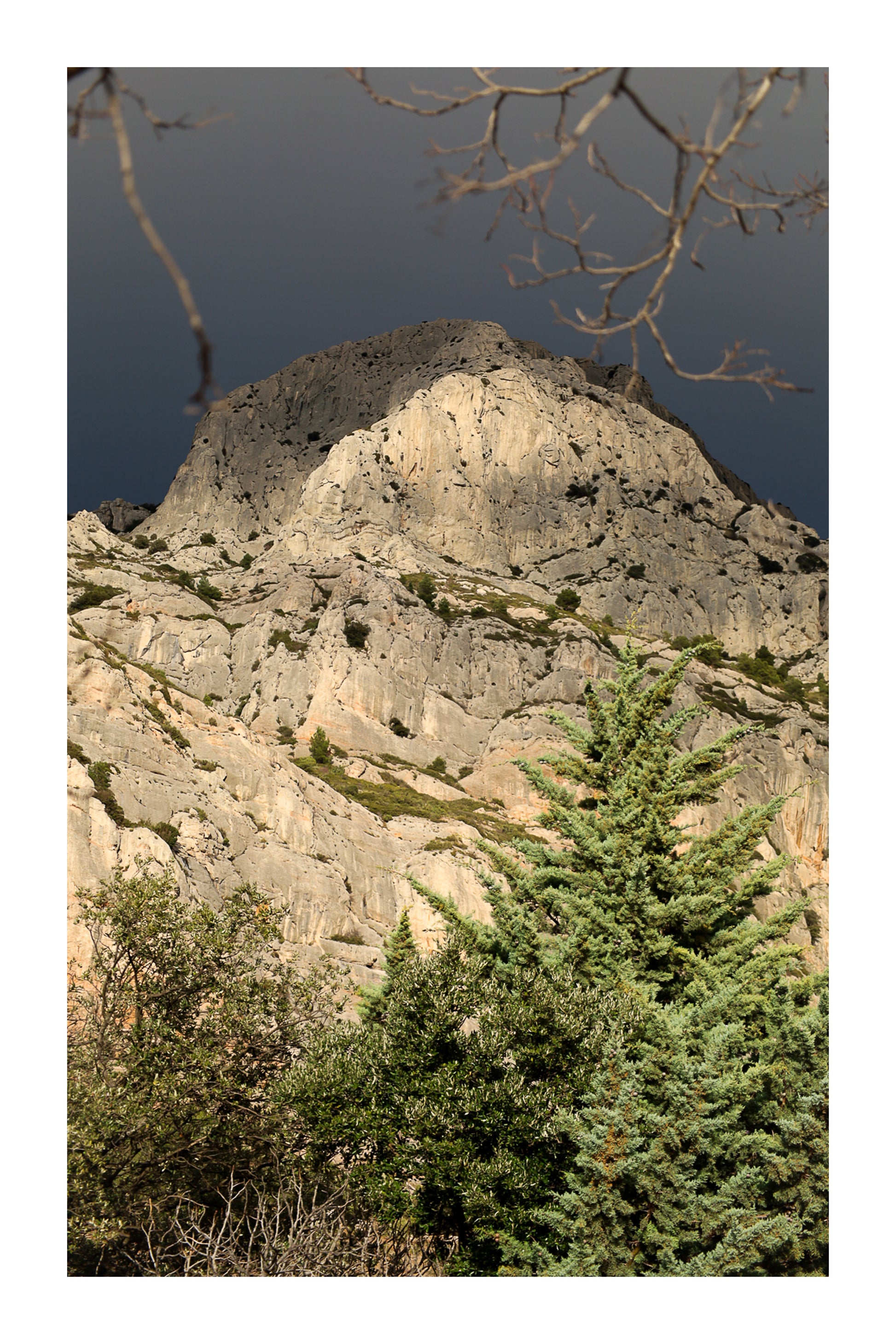 Sommet de la Sainte-Victoire encadré de branches, éclairé sur fond de ciel noir avec bordure