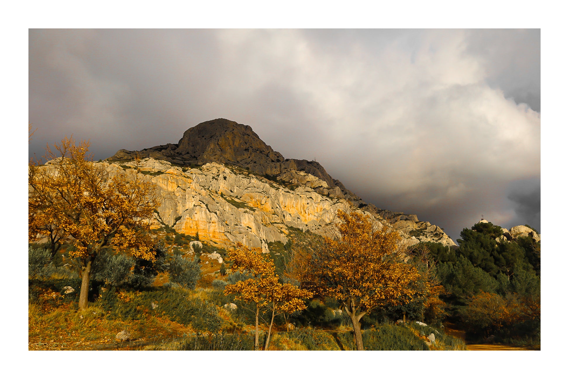 Arbres d’automne dorés devant la falaise claire de la Sainte-Victoire et un ciel gris avec bordure