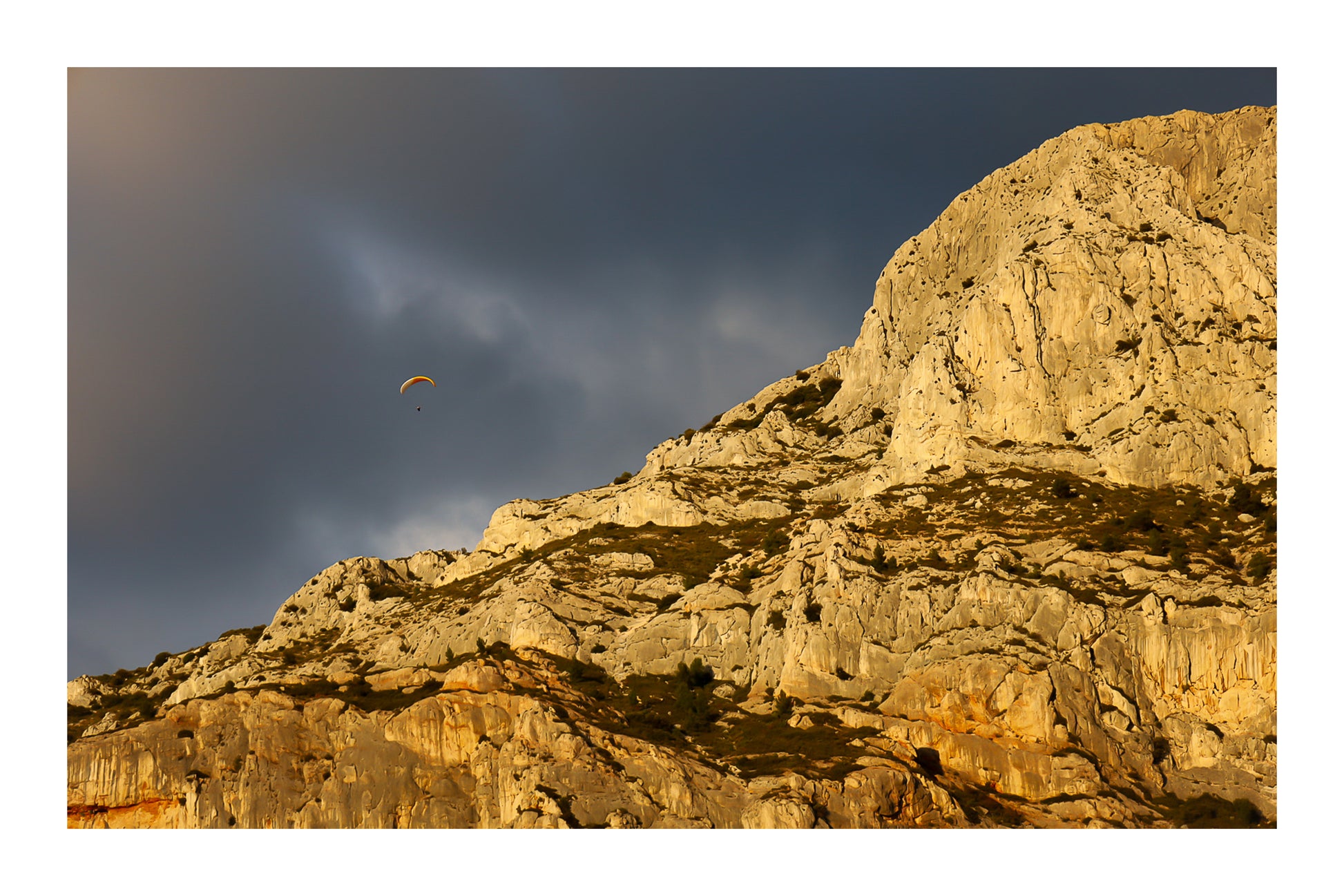 Parapente dans le ciel sombre au-dessus des falaises claires de la Sainte-Victoire avec bordure