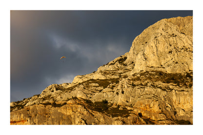 Parapente dans le ciel sombre au-dessus des falaises claires de la Sainte-Victoire avec bordure