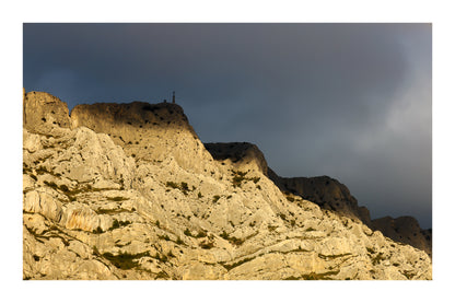 Croix de la Sainte-Victoire éclairée par le soleil sur fond de nuages sombres avec bordure