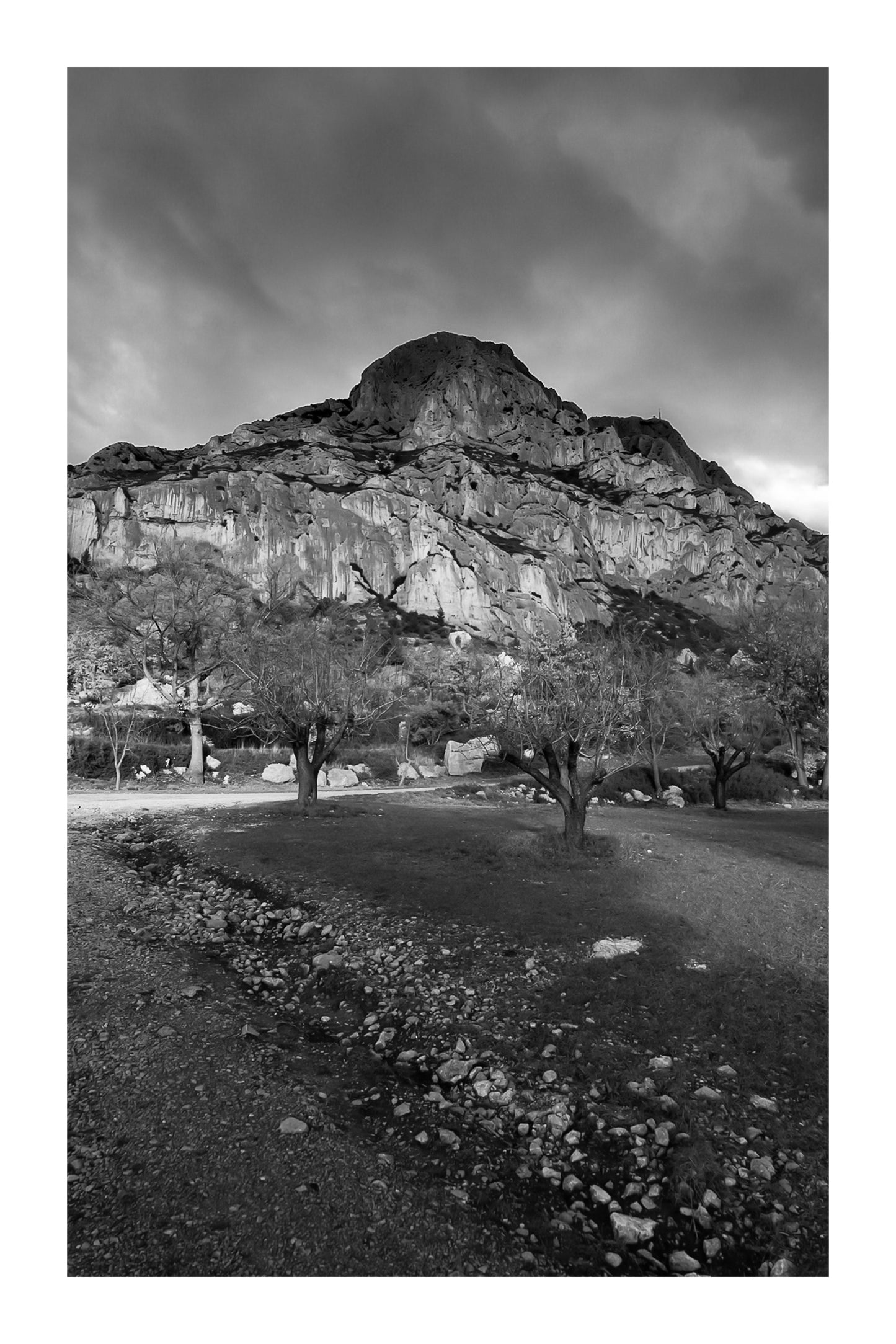 Amandiers au pied de la Sainte-Victoire illuminée par un ciel orageux bleu profond, noir et blanc avec bordure
