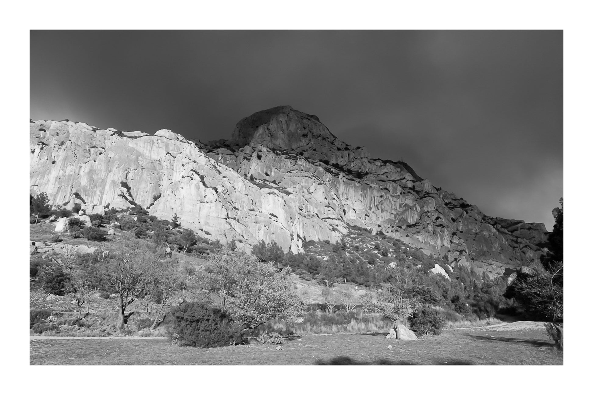 Falaise de la Sainte-Victoire dorée par le soleil avec gros nuages noirs au-dessus, noir et blanc avec bordure