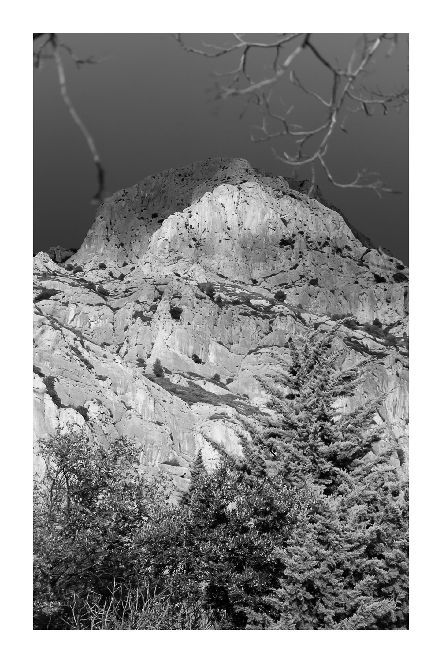 Sommet de la Sainte-Victoire encadré de branches, éclairé sur fond de ciel noir, noir et blanc avec bordure