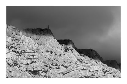 Croix de la Sainte-Victoire éclairée par le soleil sur fond de nuages sombres, noir et blanc avec bordure
