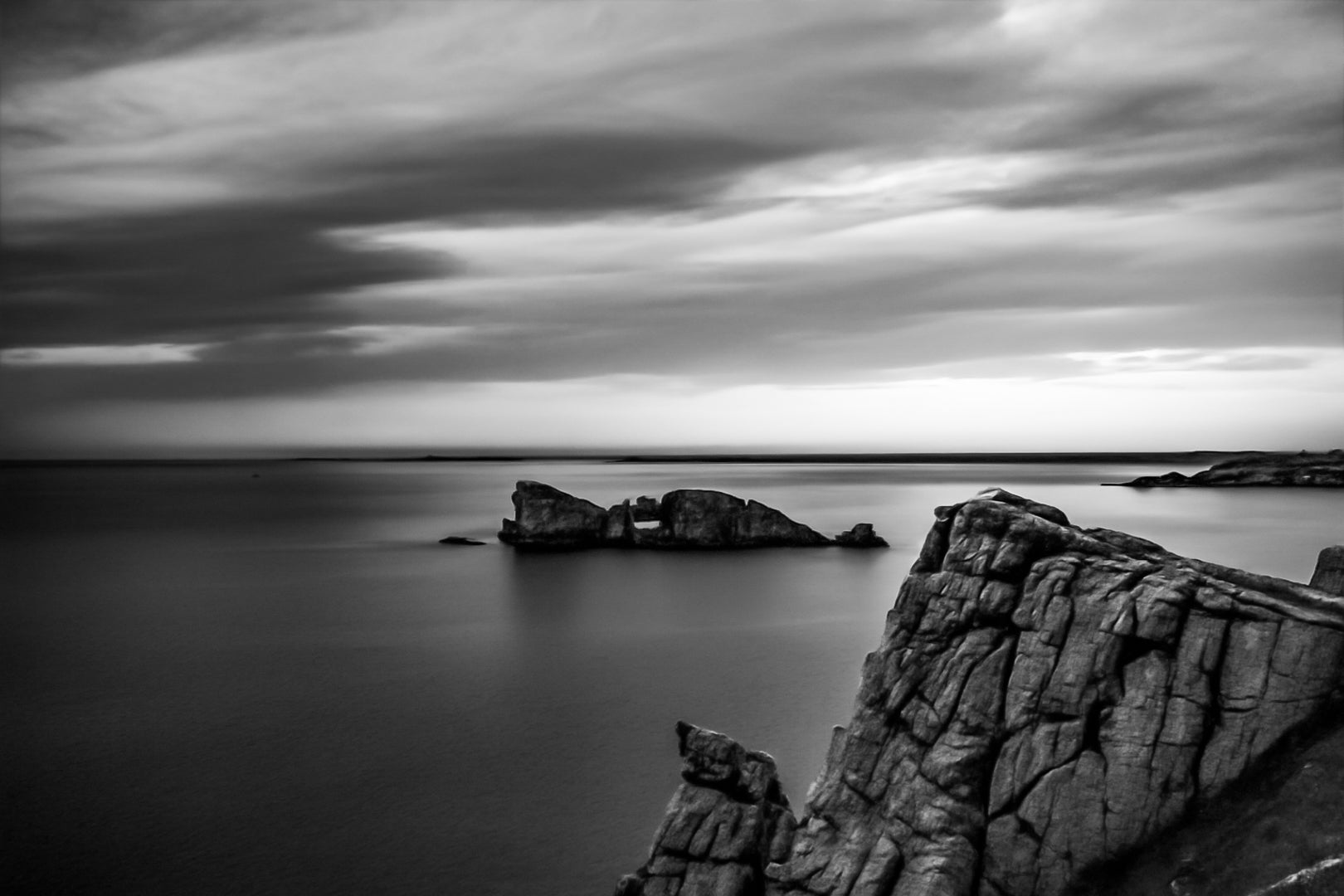 Îlot rocheux percé d’une arche au large de Pen Hir, ciel orageux et mer calme, noir et blanc