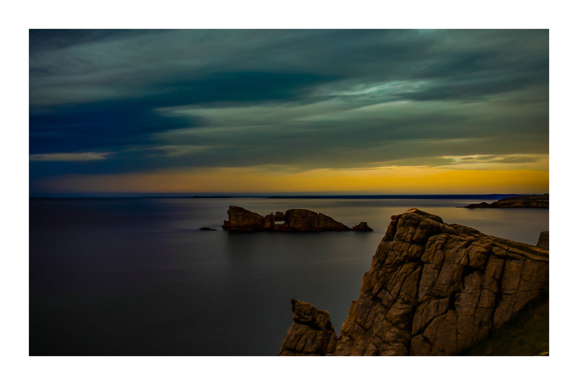Îlot rocheux percé d’une arche au large de Pen Hir, ciel orageux et mer calme avec bordure