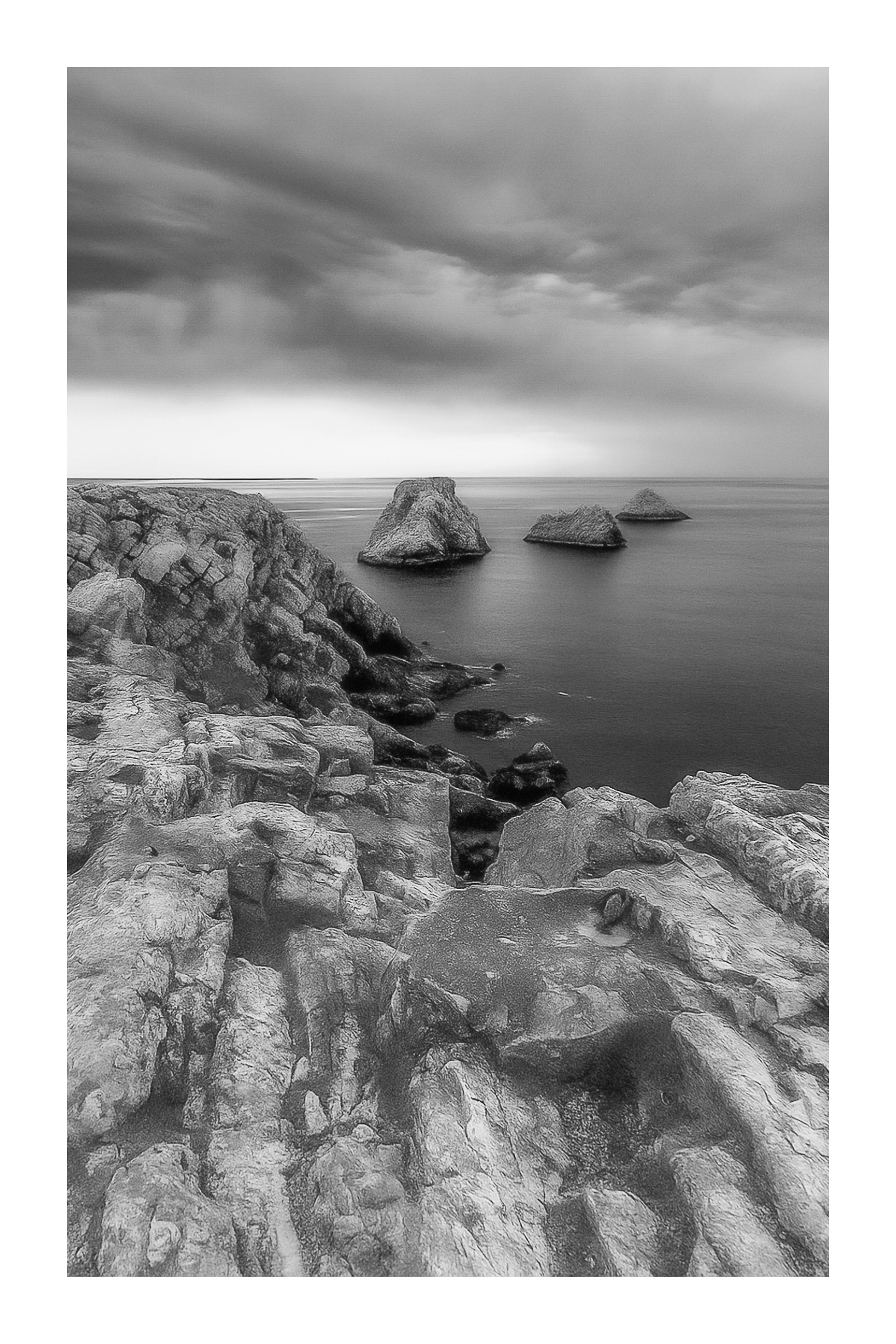 Falaises abruptes et îlots des Tas de Pois à Pen Hir sous un ciel tourmenté, noir et blanc avec bordure