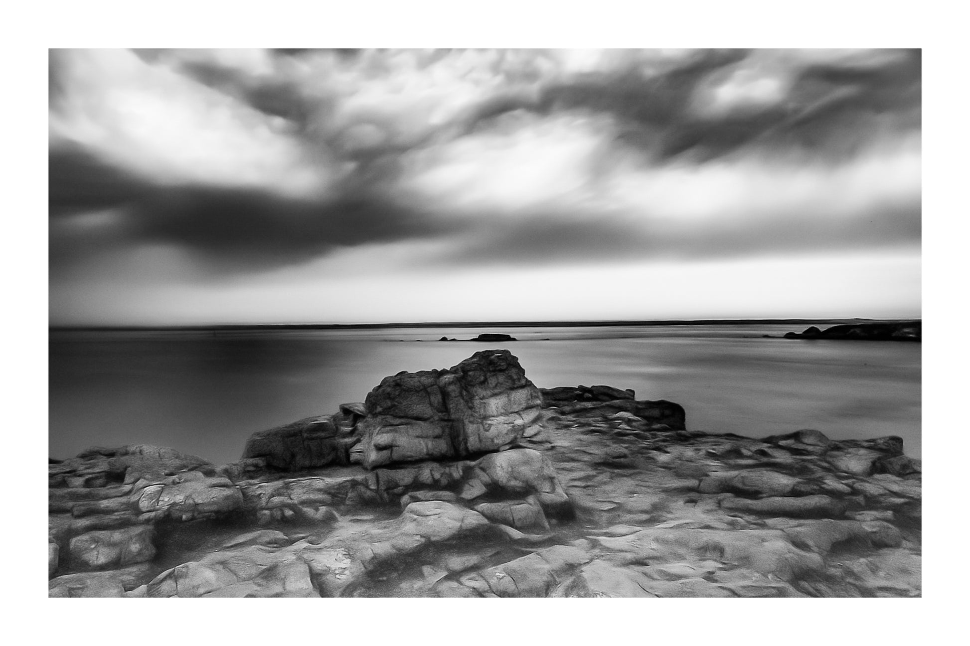 Rocher au premier plan sous un ciel d’orage coloré au cap de Pen Hir en Bretagne, noir et blanc avec bordure