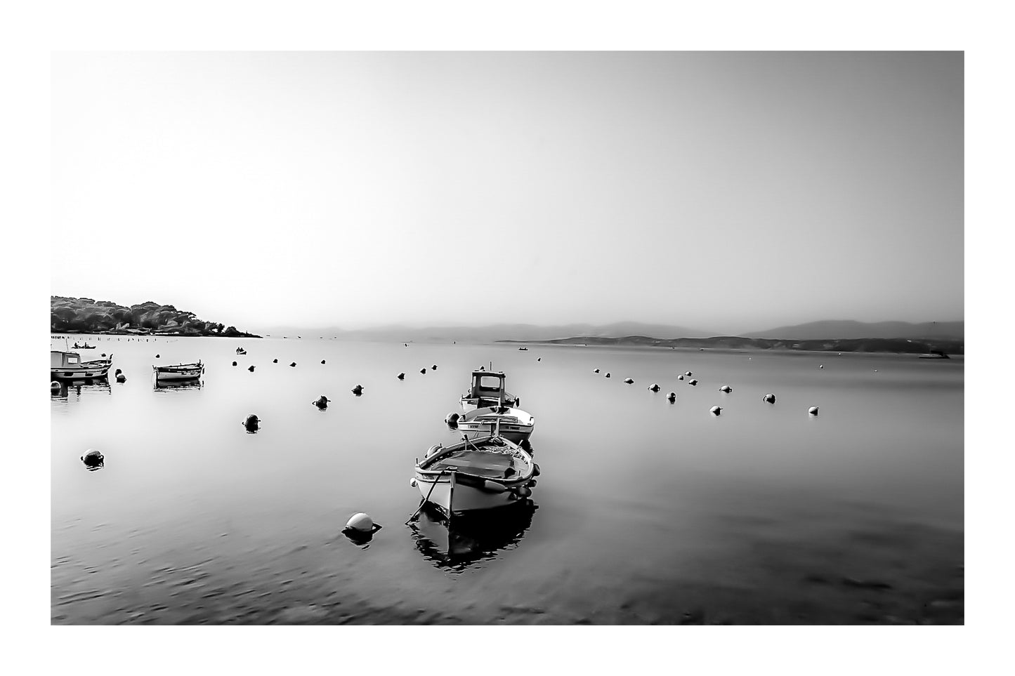 Trois barques alignées dans l’axe, bouées et eau immobile, brume et collines lointaines au Brusc, noir et blanc avec bordure