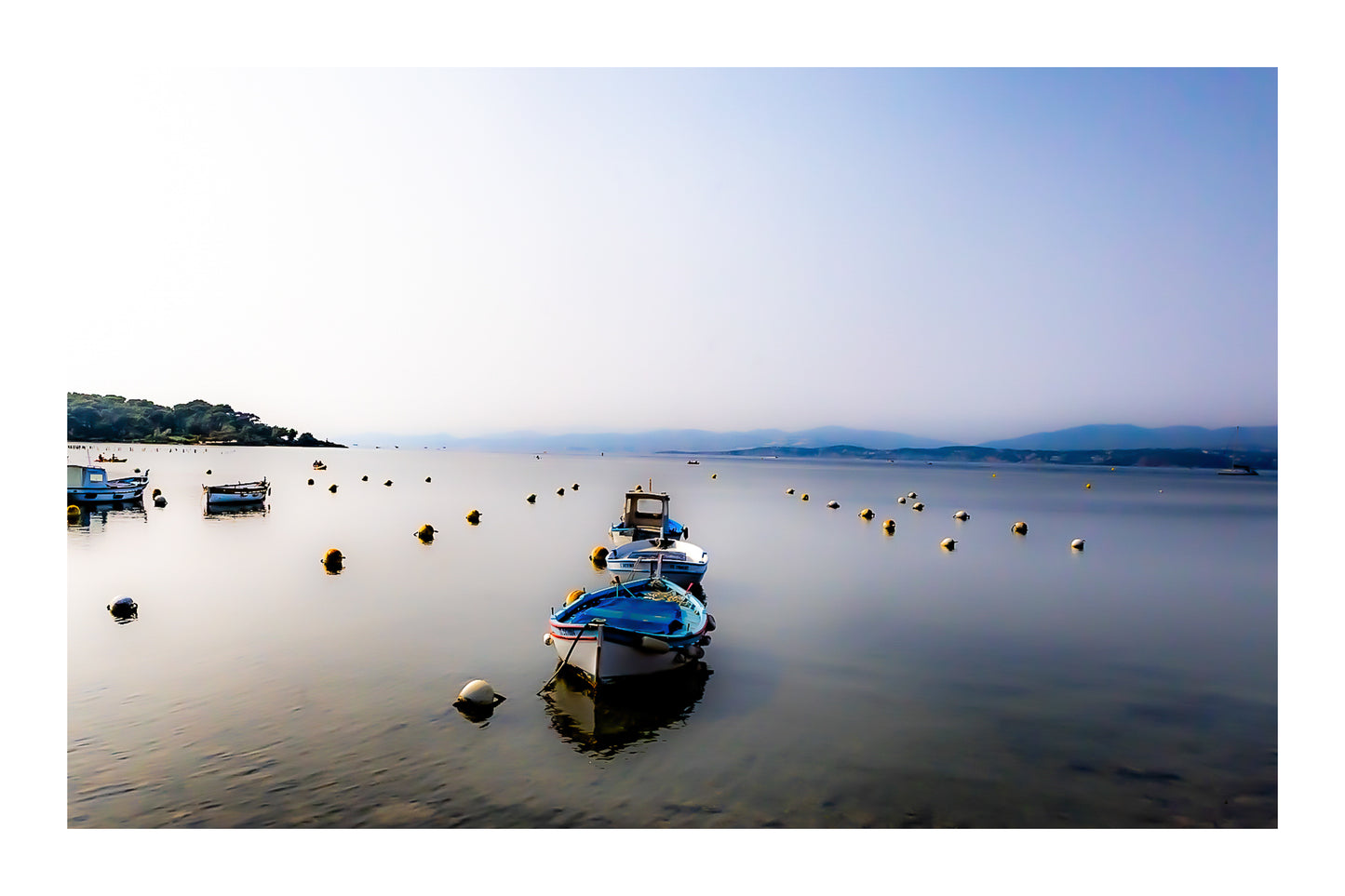 Trois barques alignées dans l’axe, bouées et eau immobile, brume et collines lointaines au Brusc, couleur avec bordure