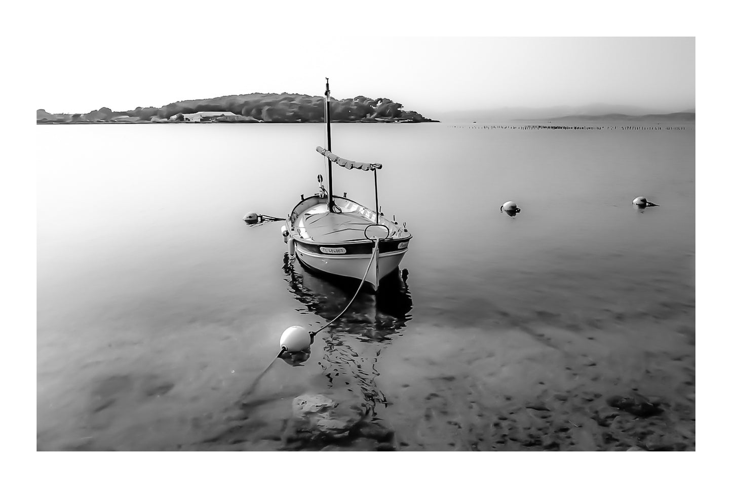 Barque solitaire amarrée avec sa aussière et bouées, reflets sur l’eau, port du Brusc, noir et blanc avec bordure