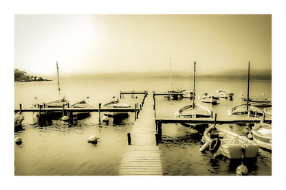 Ponton en bois menant à une rangée de barques, mer lisse et brume douce au port du Brusc, look vintage sépia avec bordure