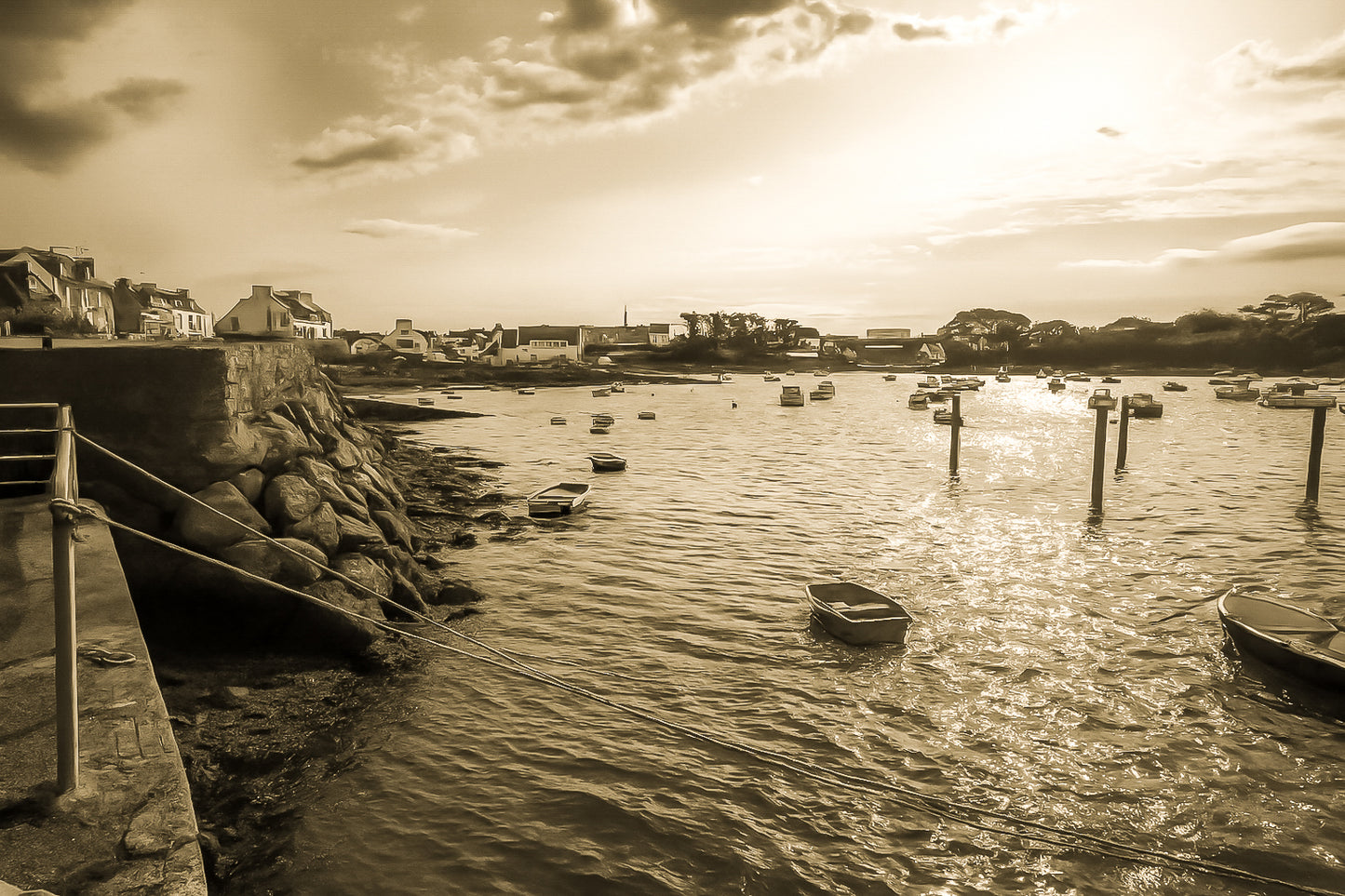 Vue du port de Portsall au coucher du soleil, muret de pierre et rochers au premier plan, petites barques au mouillage sur mer dorée, vintage