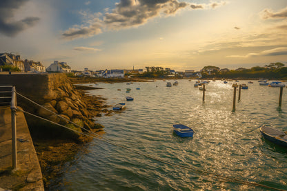 Vue du port de Portsall au coucher du soleil, muret de pierre et rochers au premier plan, petites barques au mouillage sur mer dorée