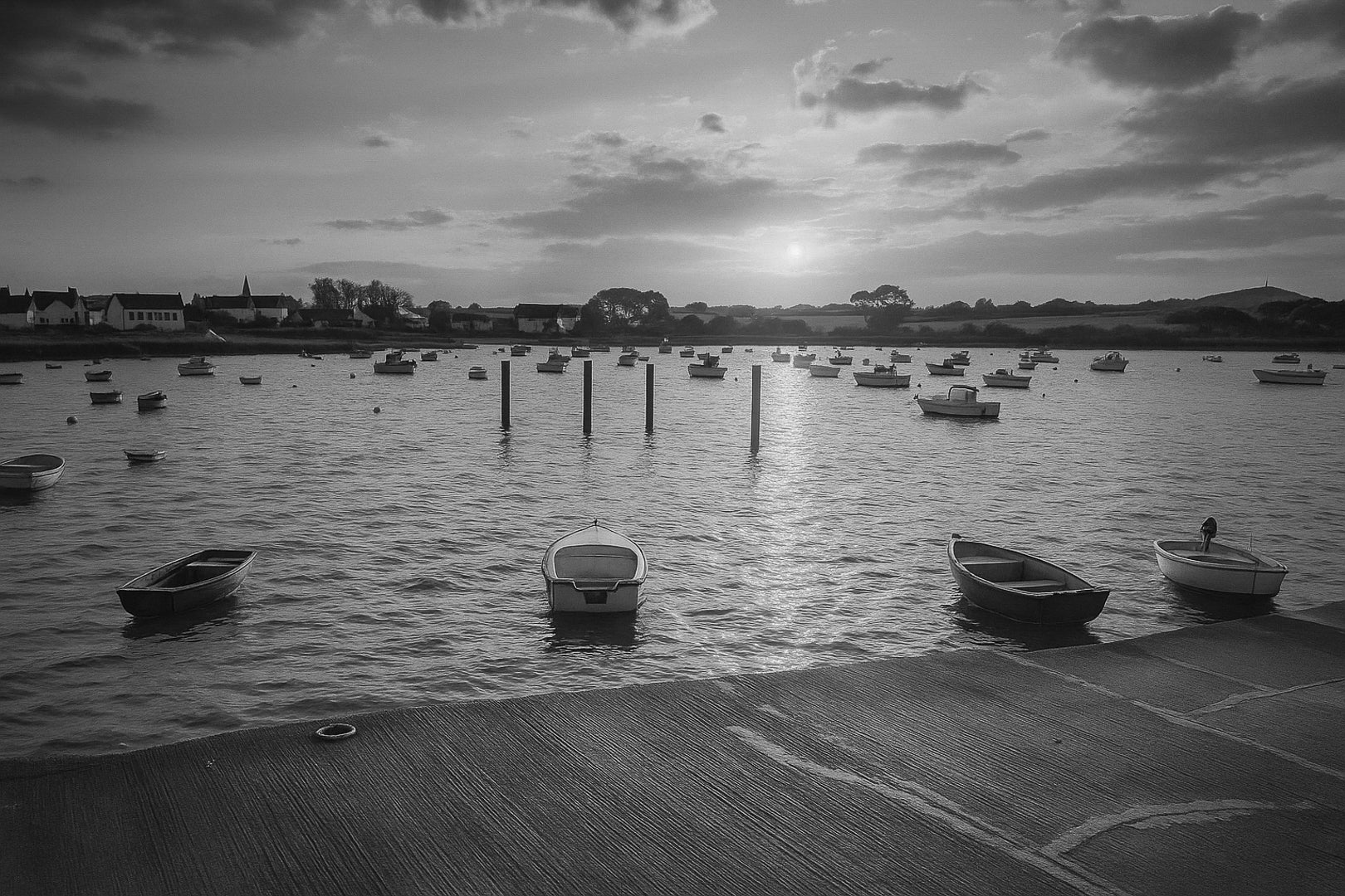 Petites embarcations alignées à Portsall, soleil rasant et rangées de bouées, reflets chauds sur l’eau tranquille, noir et blanc