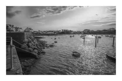Vue du port de Portsall au coucher du soleil, muret de pierre et rochers au premier plan, petites barques au mouillage sur mer dorée, noir et blanc avec bordure