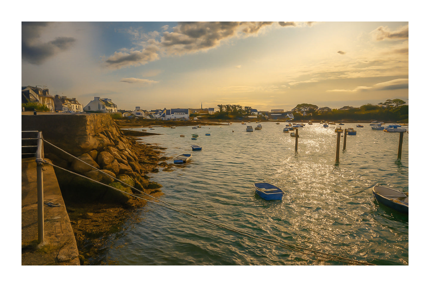 Vue du port de Portsall au coucher du soleil, muret de pierre et rochers au premier plan, petites barques au mouillage sur mer dorée, avec bordure