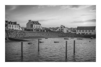 Maisons du bord de mer à Portsall baignées de lumière dorée, poteaux d’amarrage et barques dispersées sur l’anse, noir et blanc avec bordure