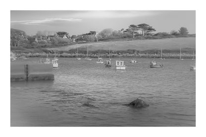 Panorama de la ria de Portsall avec nombreux bateaux au mouillage, coteau arboré en arrière-plan, lumière de fin de journée, noir et blanc avec bordure