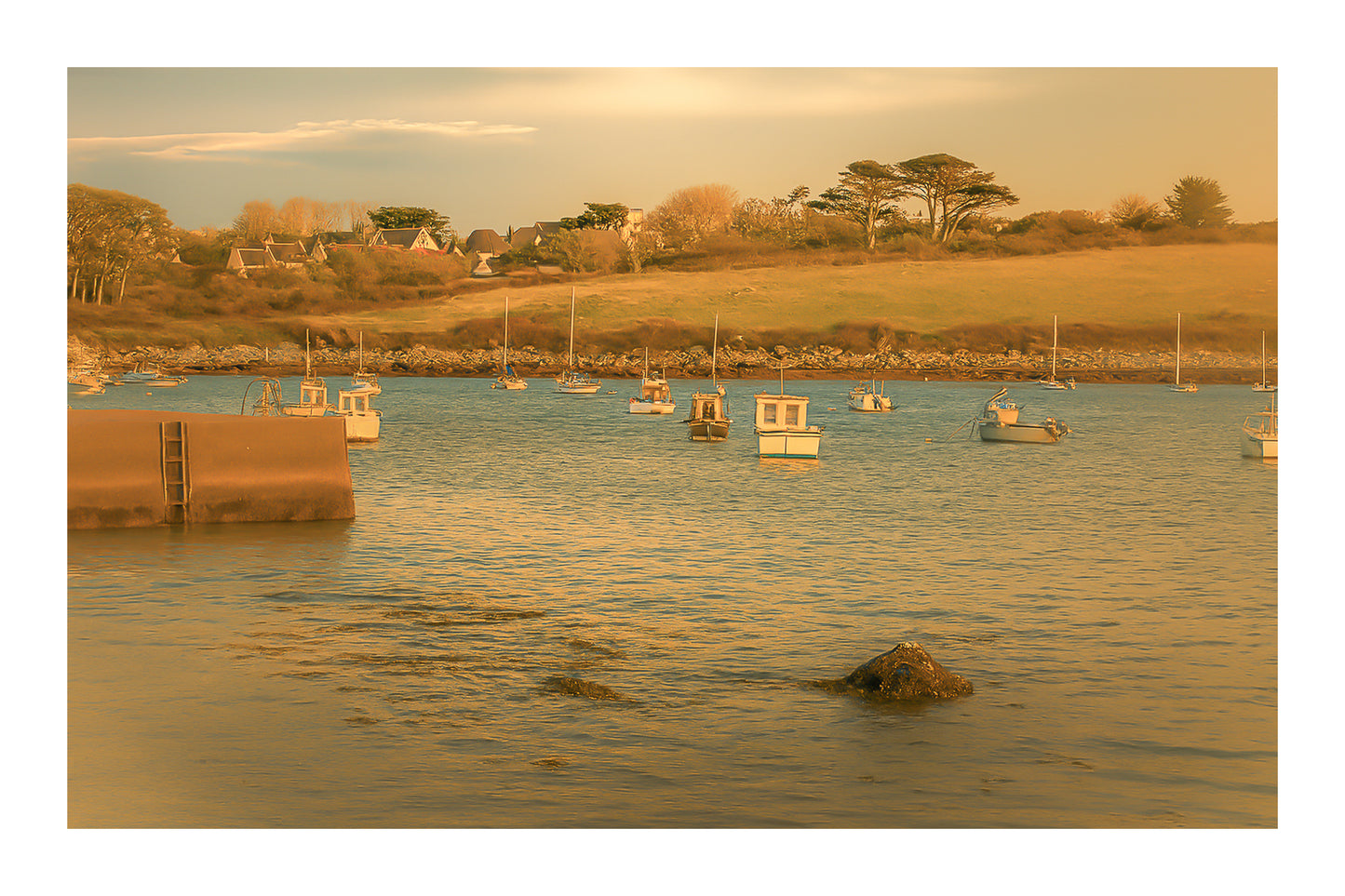 Panorama de la ria de Portsall avec nombreux bateaux au mouillage, coteau arboré en arrière-plan, lumière de fin de journée avec bordure