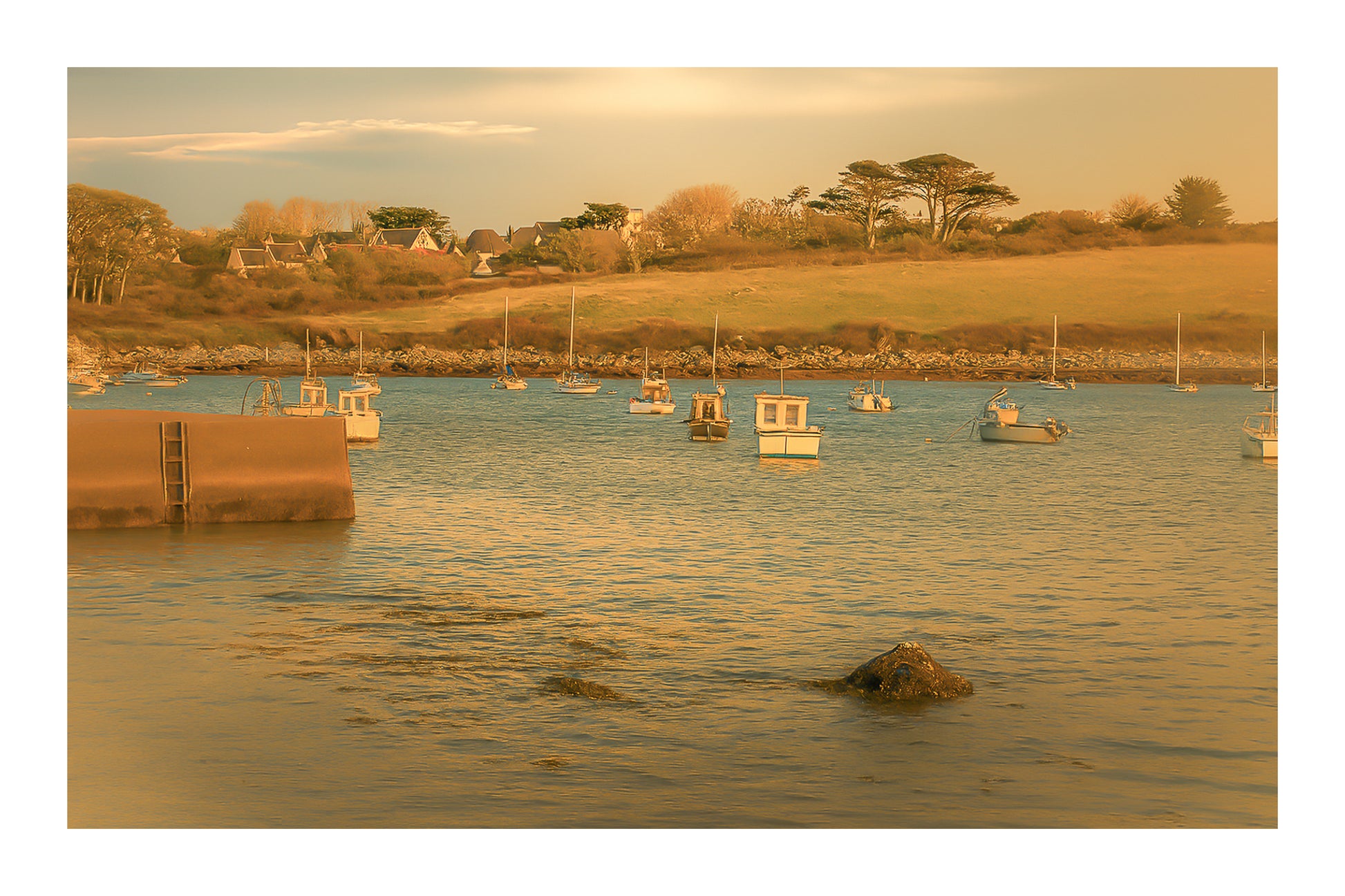 Panorama de la ria de Portsall avec nombreux bateaux au mouillage, coteau arboré en arrière-plan, lumière de fin de journée avec bordure