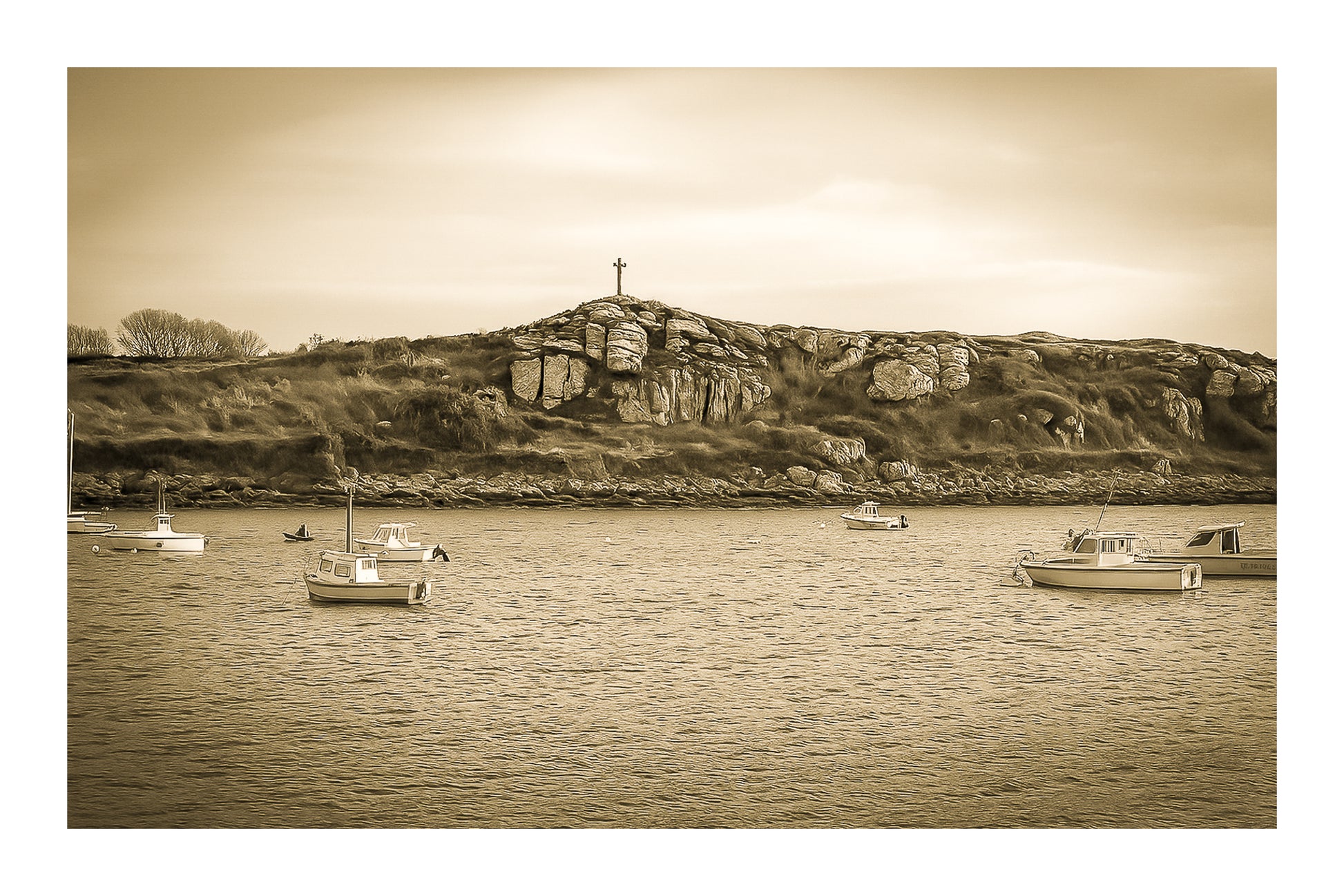 Croix dressée sur un îlot rocheux à l’entrée du port de Portsall, mer calme et bateaux épars sous un ciel doré, vintage avec bordure