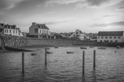 Maisons du bord de mer à Portsall baignées de lumière dorée, poteaux d’amarrage et barques dispersées sur l’anse, noir et blanc