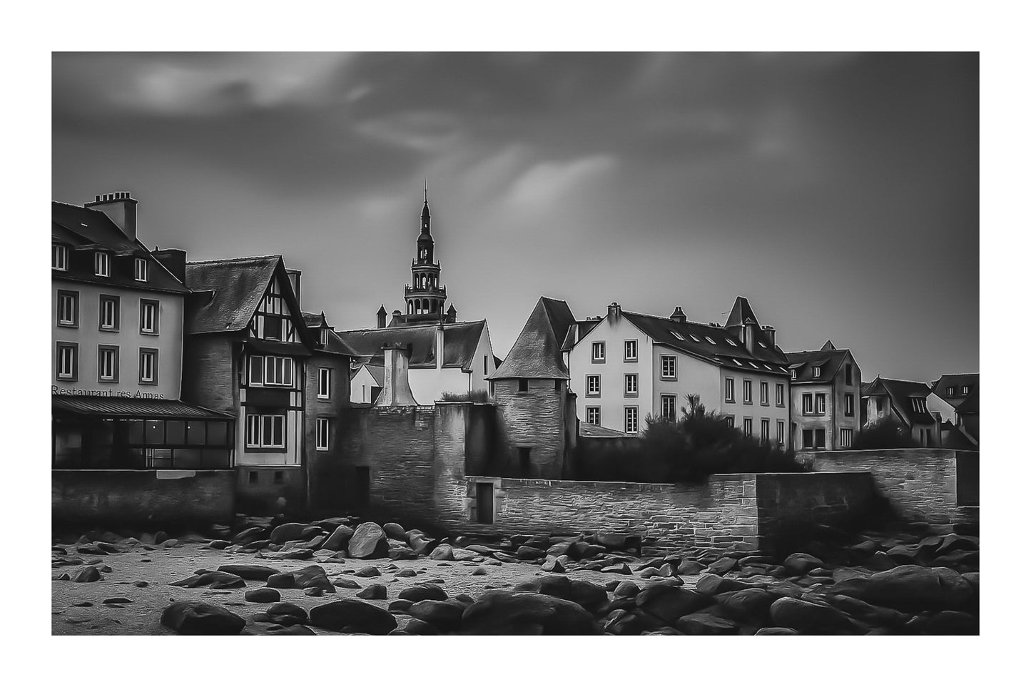 Vue sur les remparts et des maisons de Roscoff, clocher au loin et grève rocheuse au premier plan, noir et blanc avec bordure