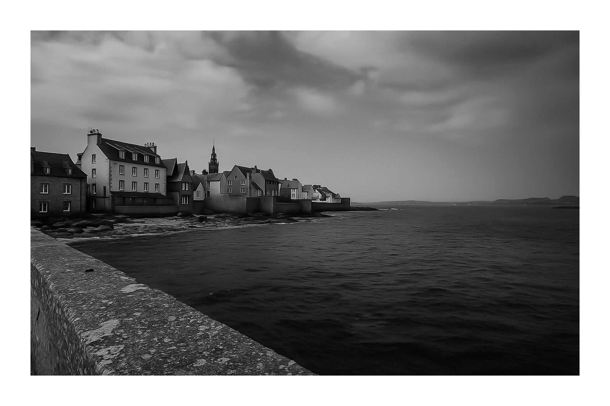 Panorama de Roscoff longeant la digue, maisons serrées au bord de l’eau face à la mer d’Iroise, noir et blanc avec bordure