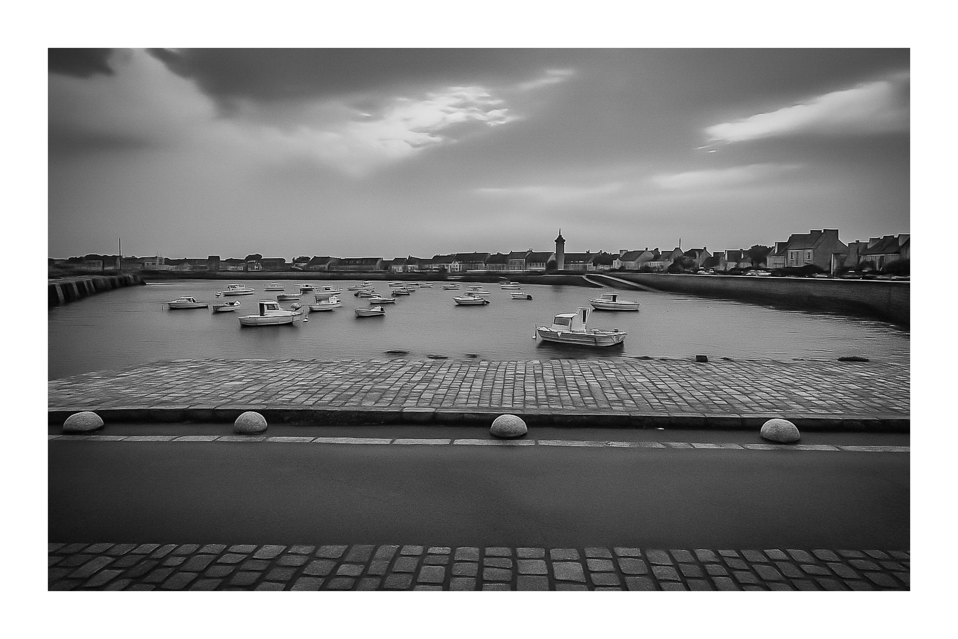 Port de Roscoff, pavés au premier plan, barques au mouillage et môle au loin, noir et blanc avec bordure